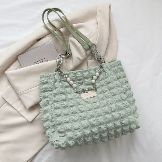 Light green textured handbag with pearl details on a white surface