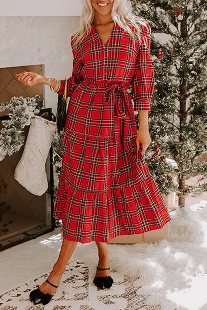 Woman wearing a red plaid dress in a festive indoor setting with a Christmas tree.